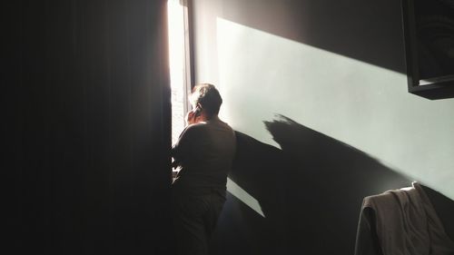 Rear view of woman talking over phone while standing by window