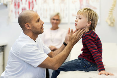 Side view of male doctor checking boy's throat at clinic