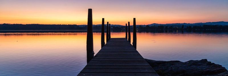 Pier over lake against sky during sunset