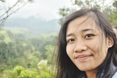 Close-up portrait of woman with tousled hair against trees