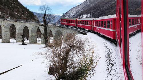 Train on snow covered bridge by mountains during winter