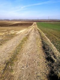 Dirt road amidst field against sky