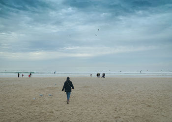Rear view of people on beach against sky