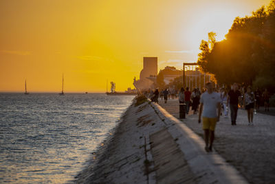 Rear view of people walking on street against sky during sunset