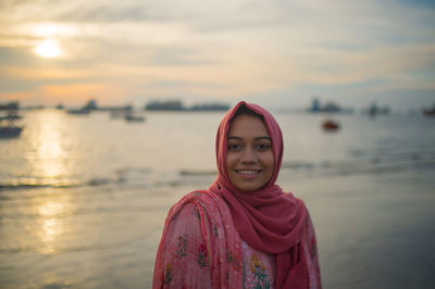 Portrait of smiling young woman standing against sky during sunset