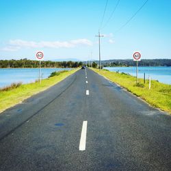 Road leading towards sign against sky