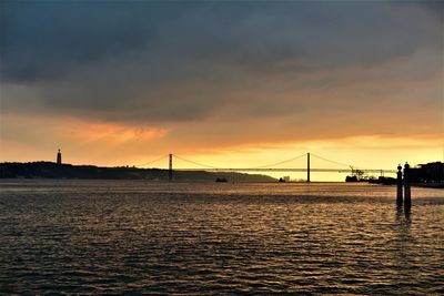 View of suspension bridge over river against cloudy sky