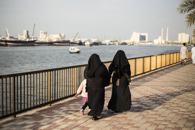 Rear view of people walking by railing against harbor