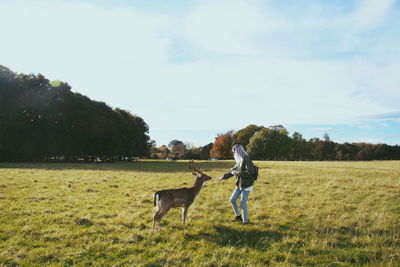 Woman with deer on landscape against sky