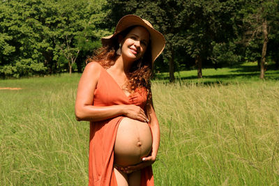 Beautiful pregnant young woman in hat standing on field