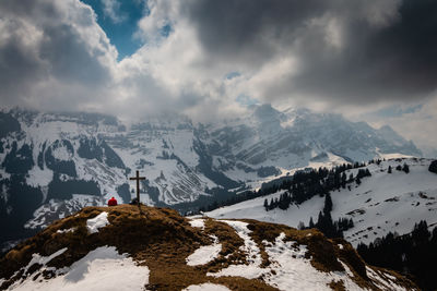 Rear view of woman sitting on snow covered mountains against cloudy sky