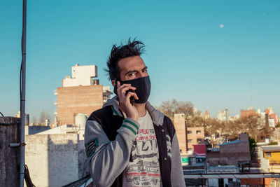 Portrait of young man with face mask in city against clear sky