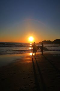 Two silhouette people with surfboards on beach at sunset