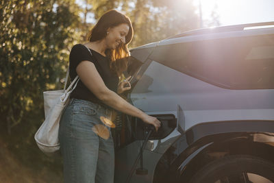 Smiling mature woman charging car while standing at station