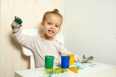 Portrait of smiling girl with painted hands sitting at table in home