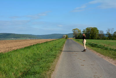Young girl rides a skateboard on a country road in nature with copy space and blue sky