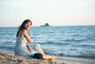 Portrait of woman sitting at beach against sky