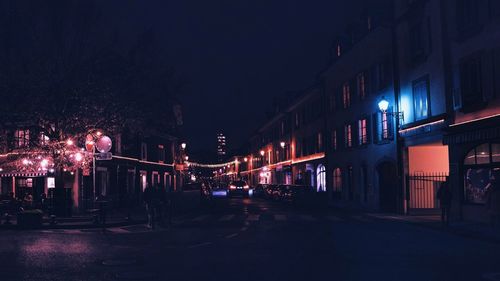 Illuminated street amidst buildings against sky at night