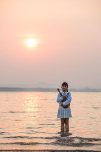 Girl with violin standing in sea against sky