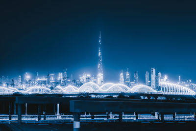 Illuminated bridge and buildings against sky at night