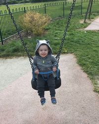 Portrait of cute boy sitting on swing in playground
