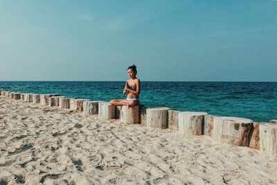 Woman sitting on beach against clear sky