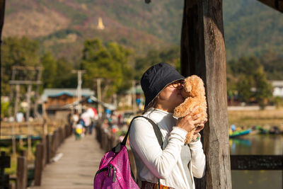 Young woman kissing stuffed toy while standing on pier