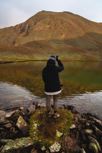 Travel photographer taking pictures of nature on a smartphone, mountain landscape by the lake person