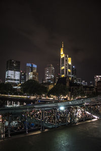 Illuminated buildings by river against sky at night