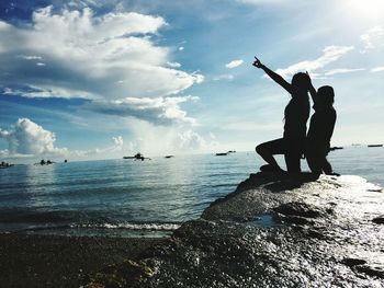 Silhouette people gesturing on seashore against sky