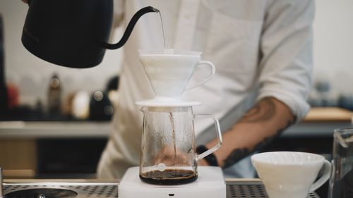 Midsection of barista pouring hot water in container at cafe