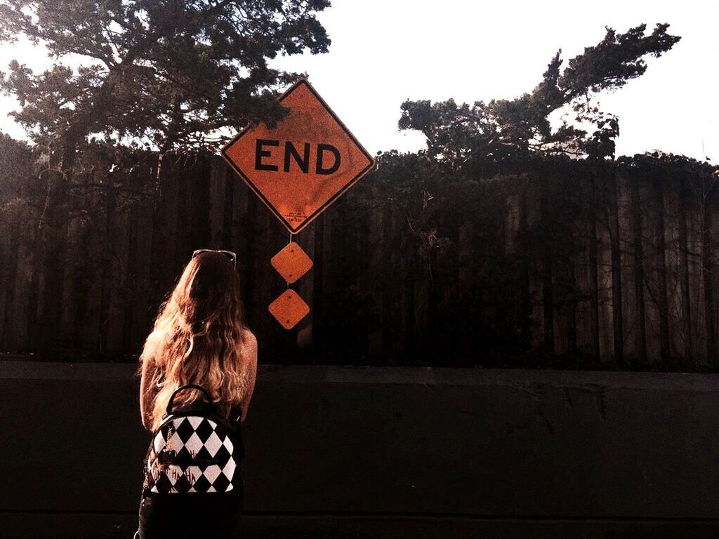 rear view, text, communication, real people, one person, tree, standing, road sign, outdoors, women, day, lifestyles, nature, one woman only, one young woman only, people