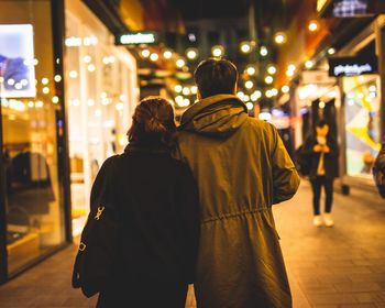 Rear view of couple standing on illuminated street at night