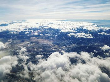 High angle view of cloudscape against sky looking through clouds to city and mountains below