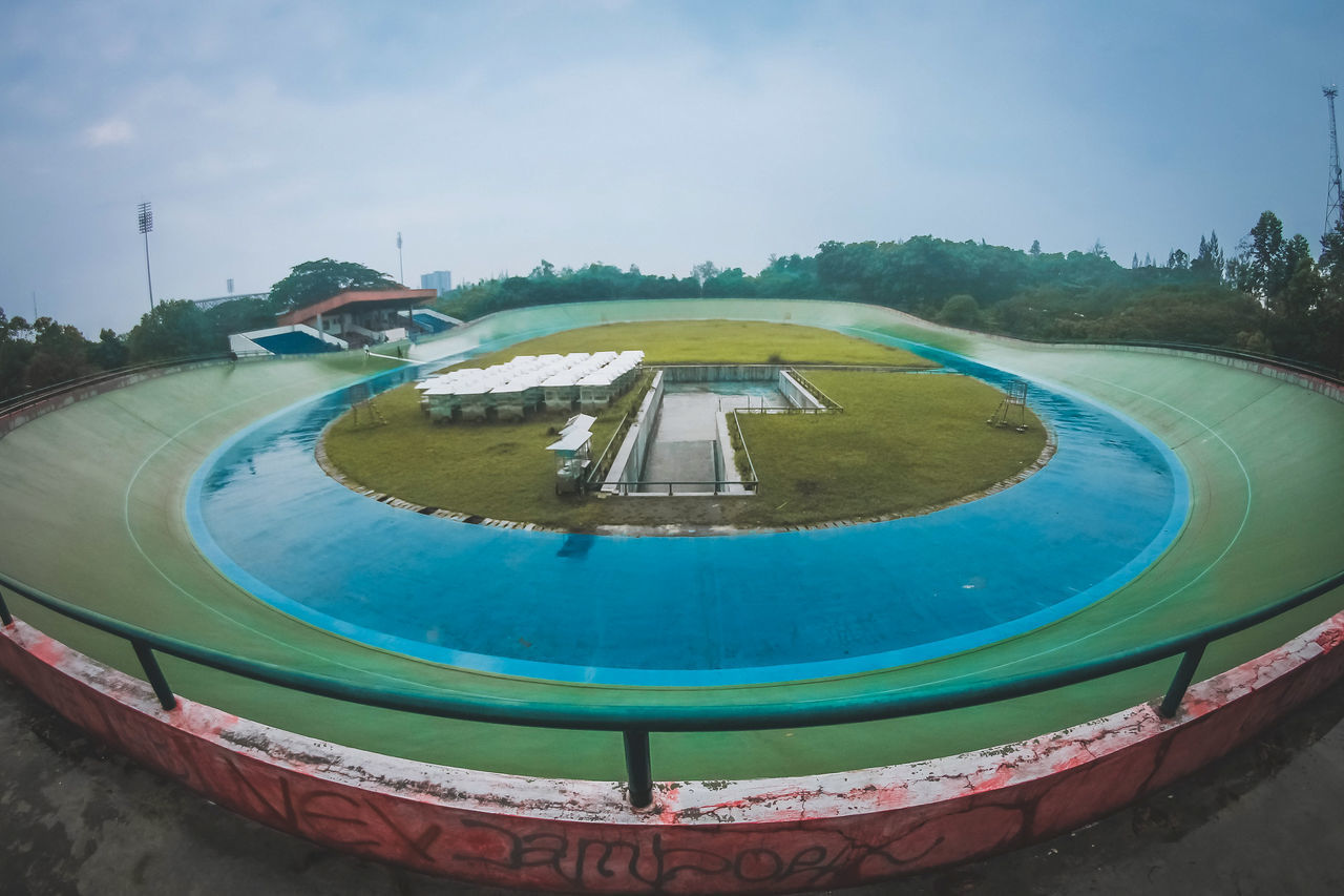 HIGH ANGLE VIEW OF SWIMMING POOL BY TREES AGAINST SKY