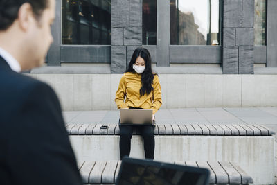 Businesspeople using laptop wearing face mask