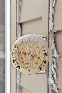 Snow covered outdoor circular thermometer shows a temperature of minus 26 degrees celsius