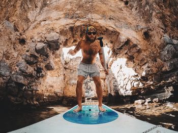 Portrait of man surfing against rock formation in sea