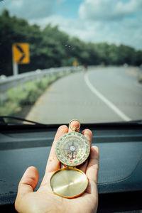 Close-up of person hand holding navigational compass by car windshield