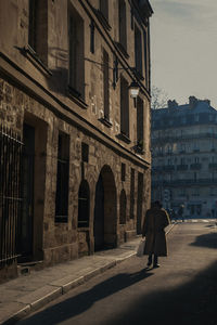 Rear view of woman walking on street amidst buildings in city