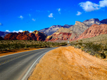 Road leading towards mountains against blue sky