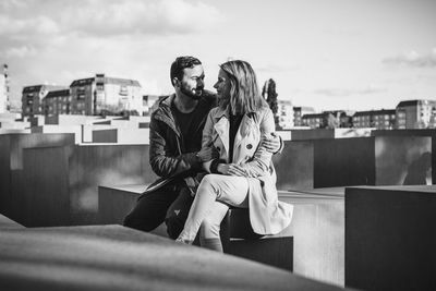 Happy young couple on retaining wall against sky in city