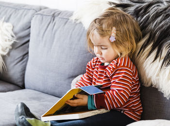 Cute girl with book sitting on sofa at home