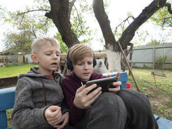 Cute boys using smart phone sitting outdoors