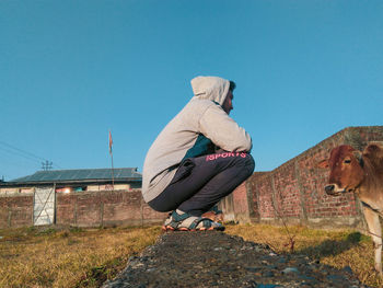 Man sitting on wall against clear blue sky