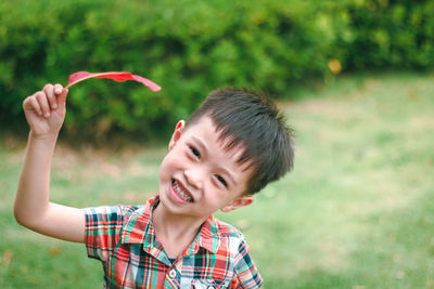 Portrait of cheerful boy holding leaf while standing on field