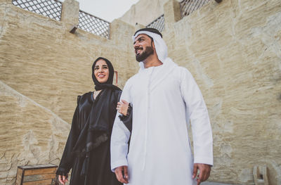 Low angle view of smiling couple standing against wall in town