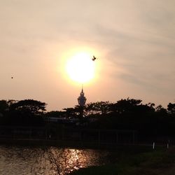 Silhouette bird flying over fountain against sky during sunset