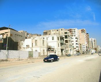 Cars on road by buildings against blue sky