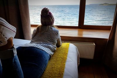 Rear view of woman sitting on window at home